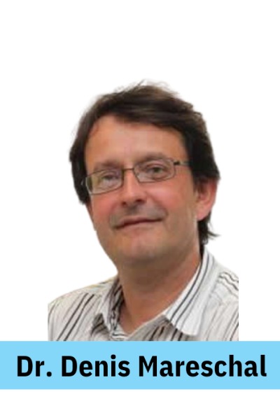 ID: A caucasian presenting man with short brown hair and thin rectangular glasses is smiling.